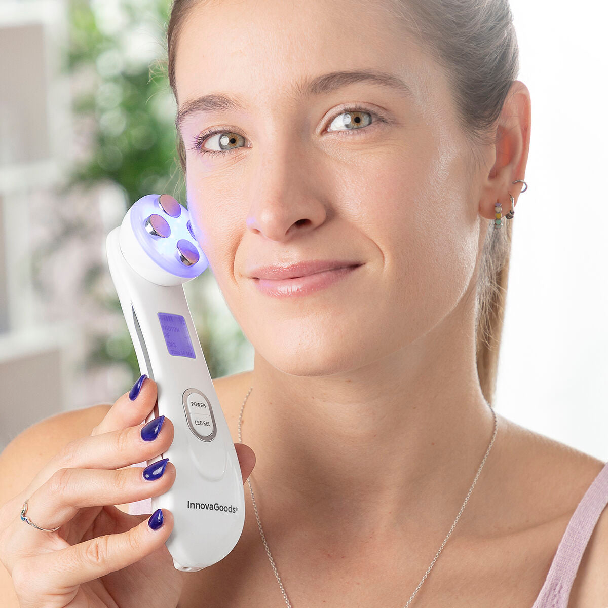 Vrouw gebruikt InnovaGoods gezichtsmassage met blauw LED-licht op wangen, helpt rimpels en fijne lijntjes te verminderen en huid te verstevigen.